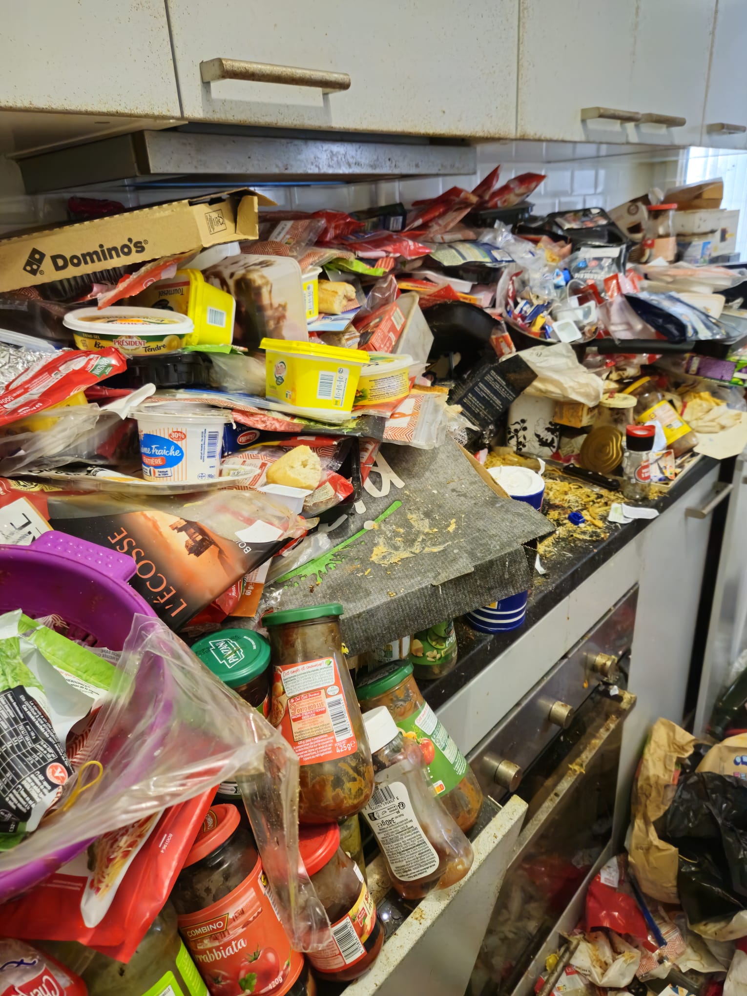 Angle cuisine avec lave-linge et amas de déchets alimentaires couvrant l'intégralité du sol