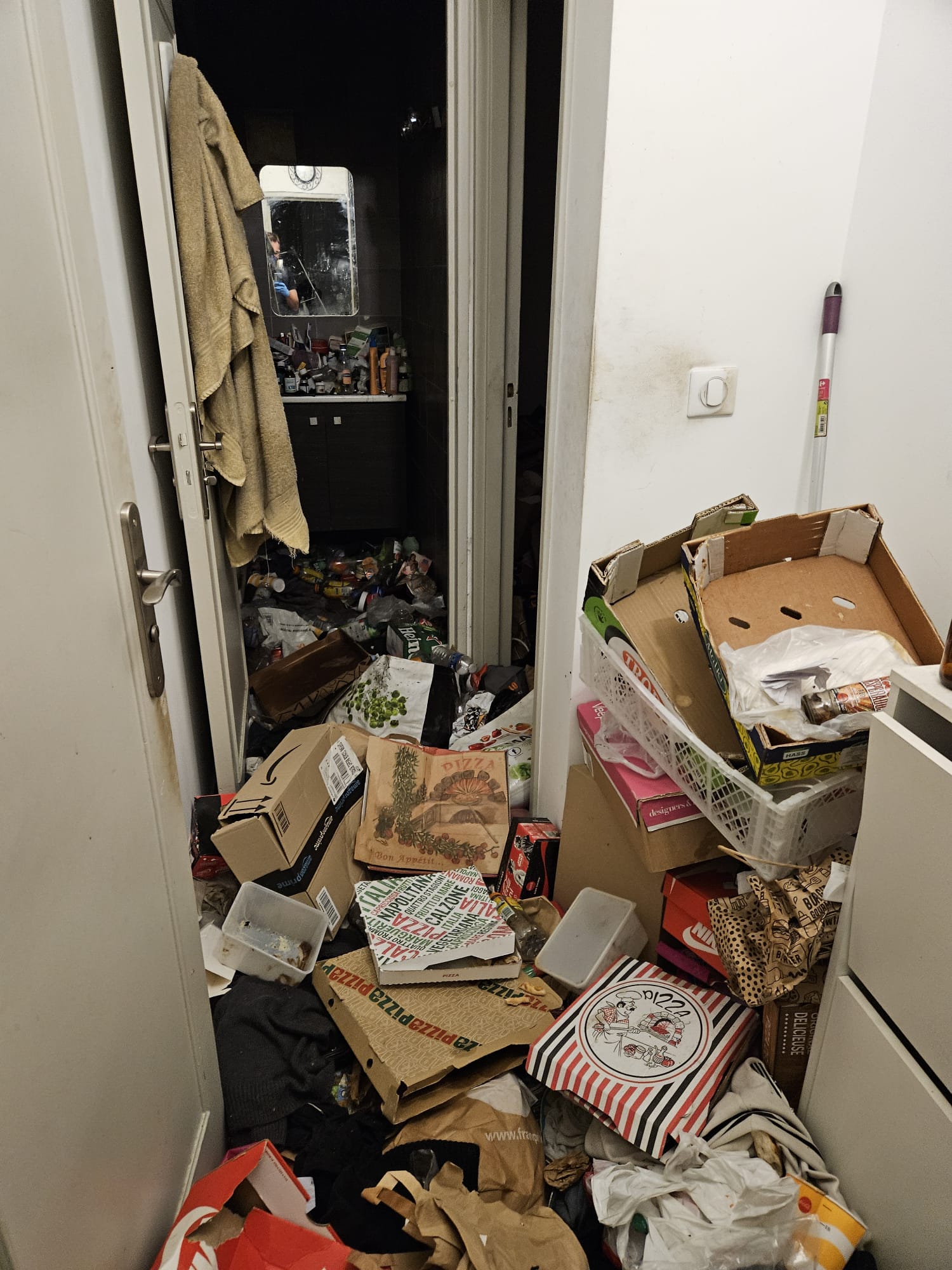 Couloir en syndrome de Diogène avant intervention : amas de cartons de pizza, sacs plastiques, emballages obstruant le passage